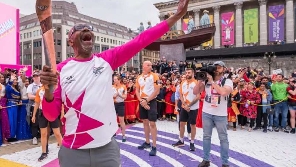 A person holding the Commonwealth baton in front of a crowd of people.