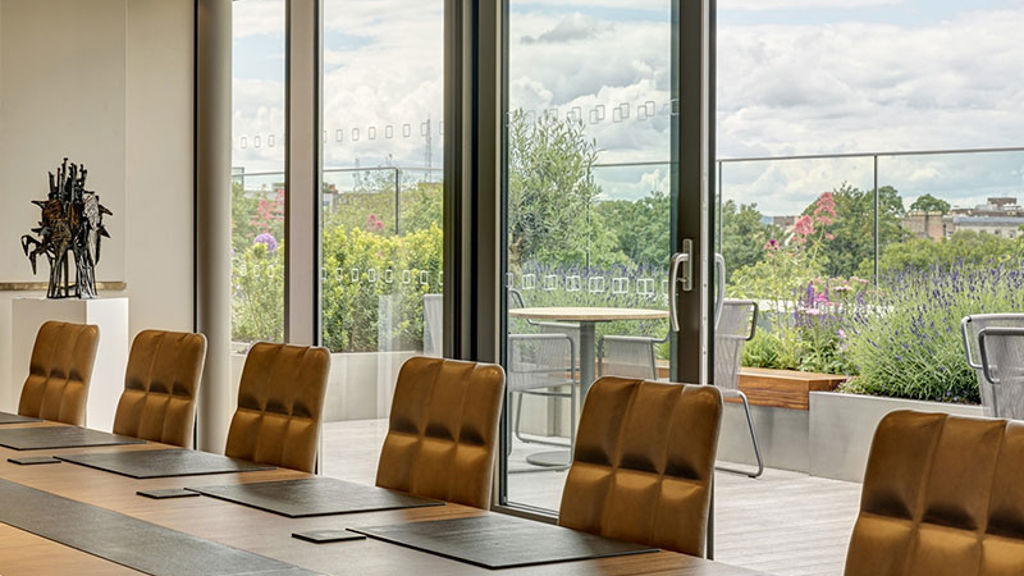A room with a table and chairs and a balcony with plants on it outside.