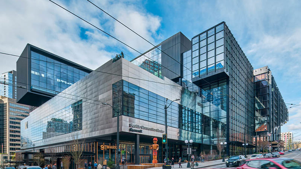 A large glass building with a street and cars in front.