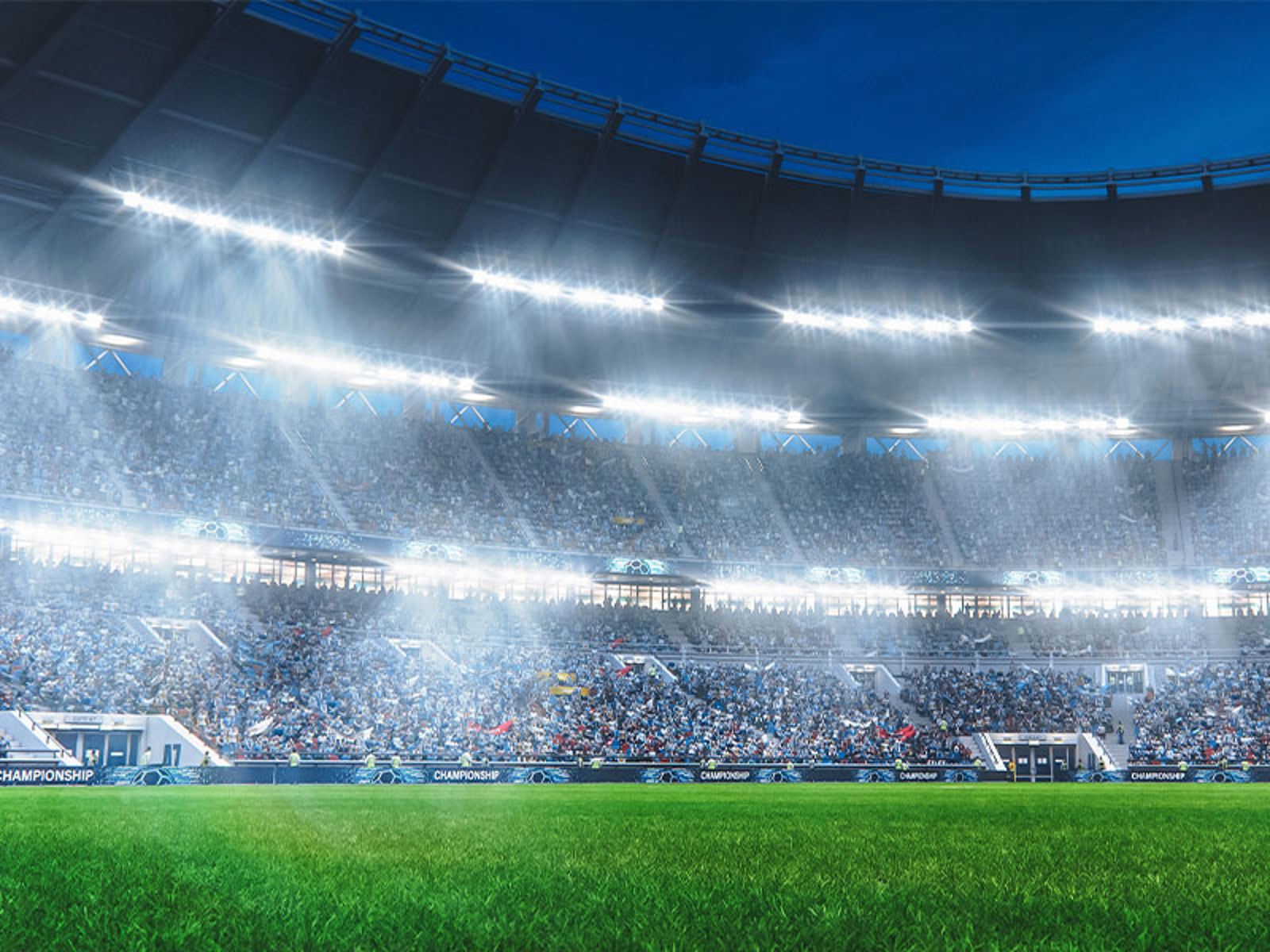 View from field of soccer stadium at night with crowd in distance and bright lights