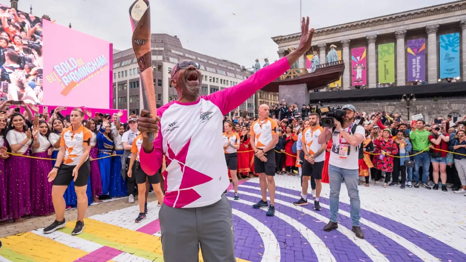 A person holding the Commonwealth baton in front of a crowd of people.