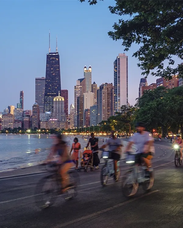 A group of people cycling on a street by a body of water in a city