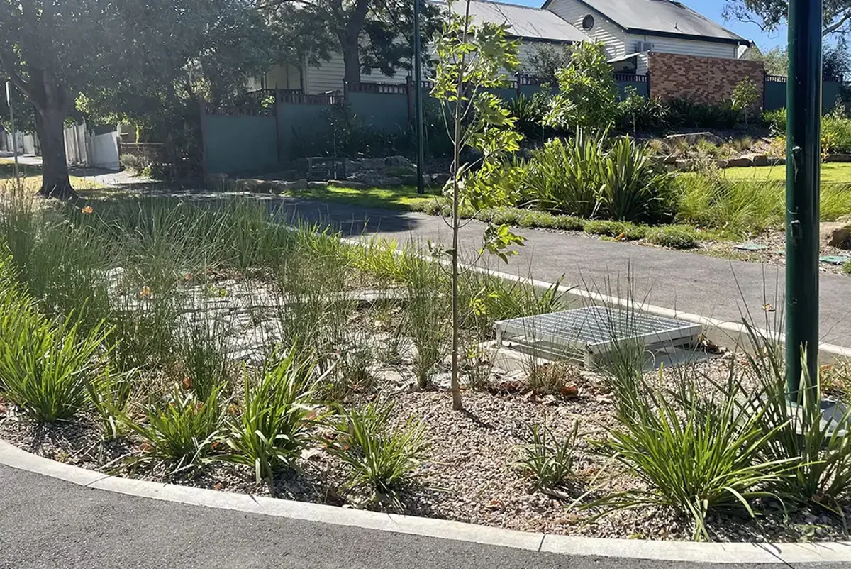 A large garden bed curbside with plantings, drainage and pebbles